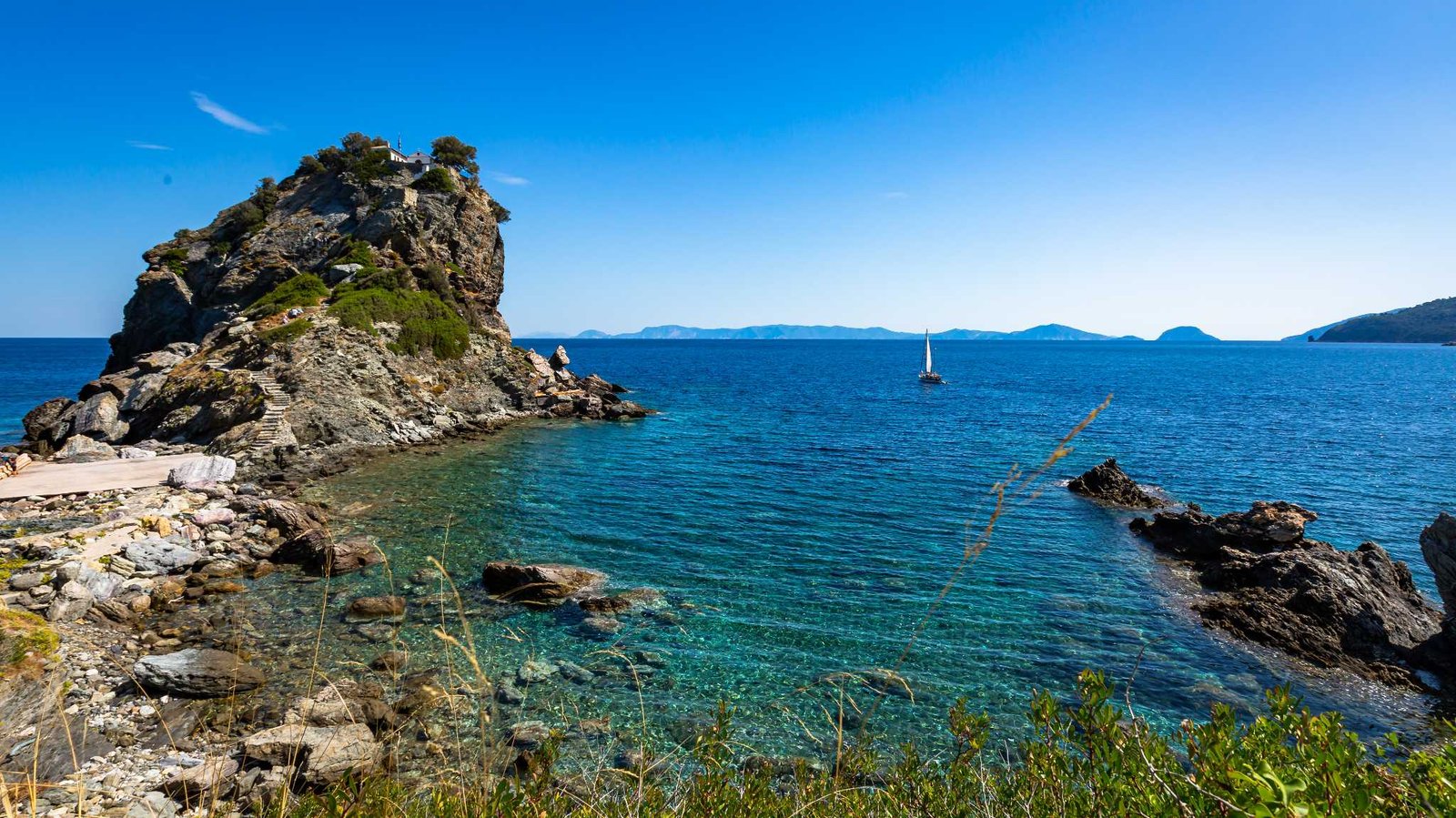 Sailboat near a rocky chapel headland in the Aegean